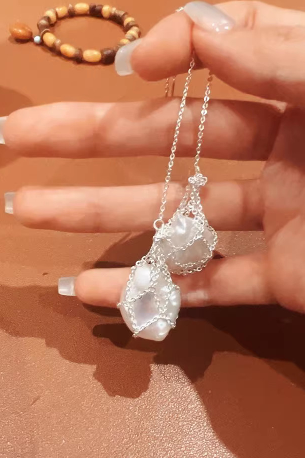 Hand holding artisanal woven pearl earrings - Natural wood bead bracelet backdrop​