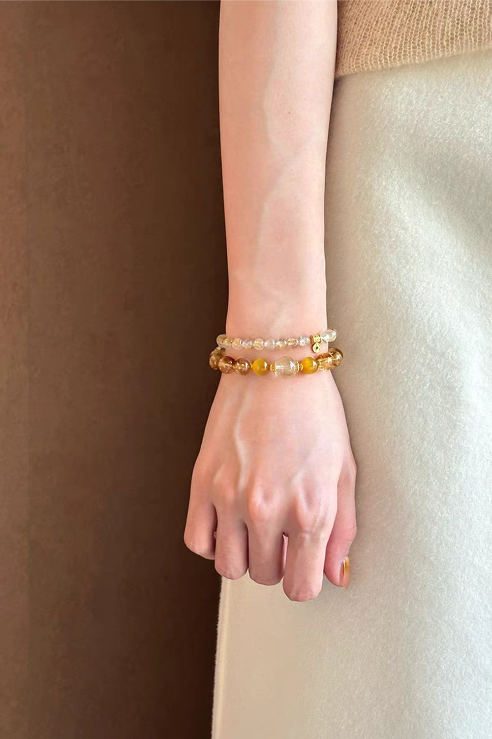 Natural crystal bracelets stacked on woman's wrist - Minimalist aesthetic with cream sweater​