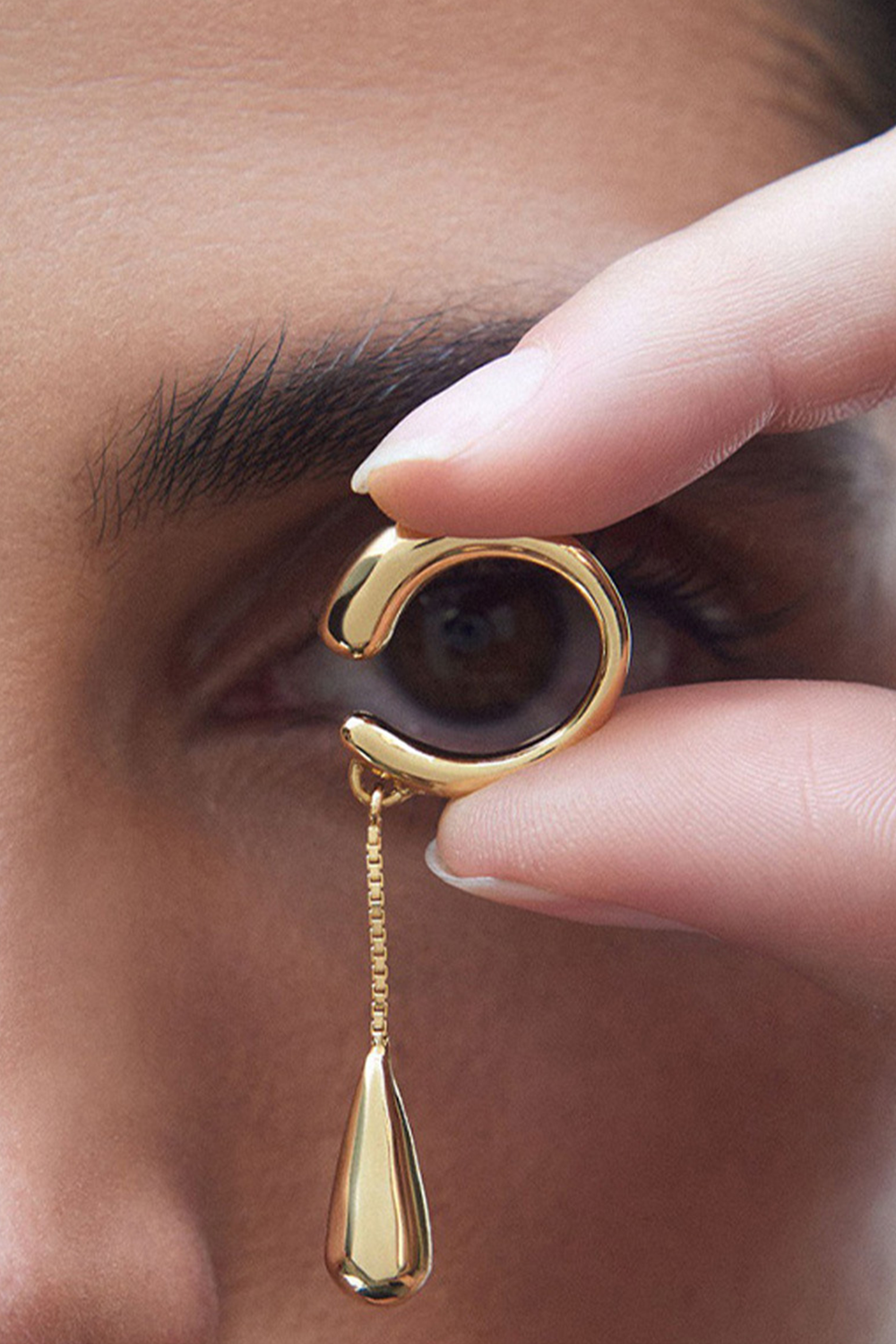 Hand holding gold open arc ear cuff near eye - Teardrop charm focus
