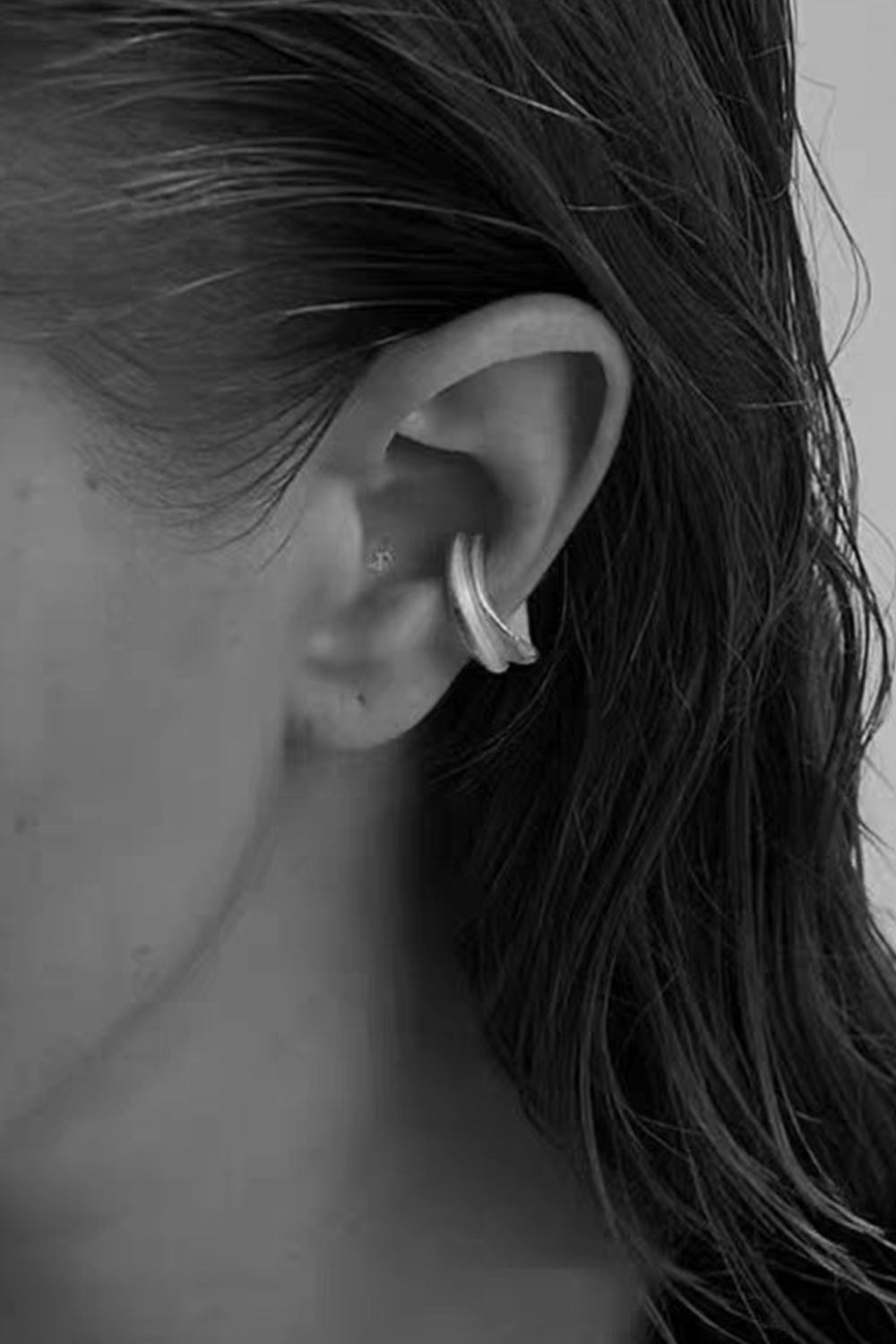 Woman's side profile wearing matte silver ear cuff - Brown hair & black top on white background