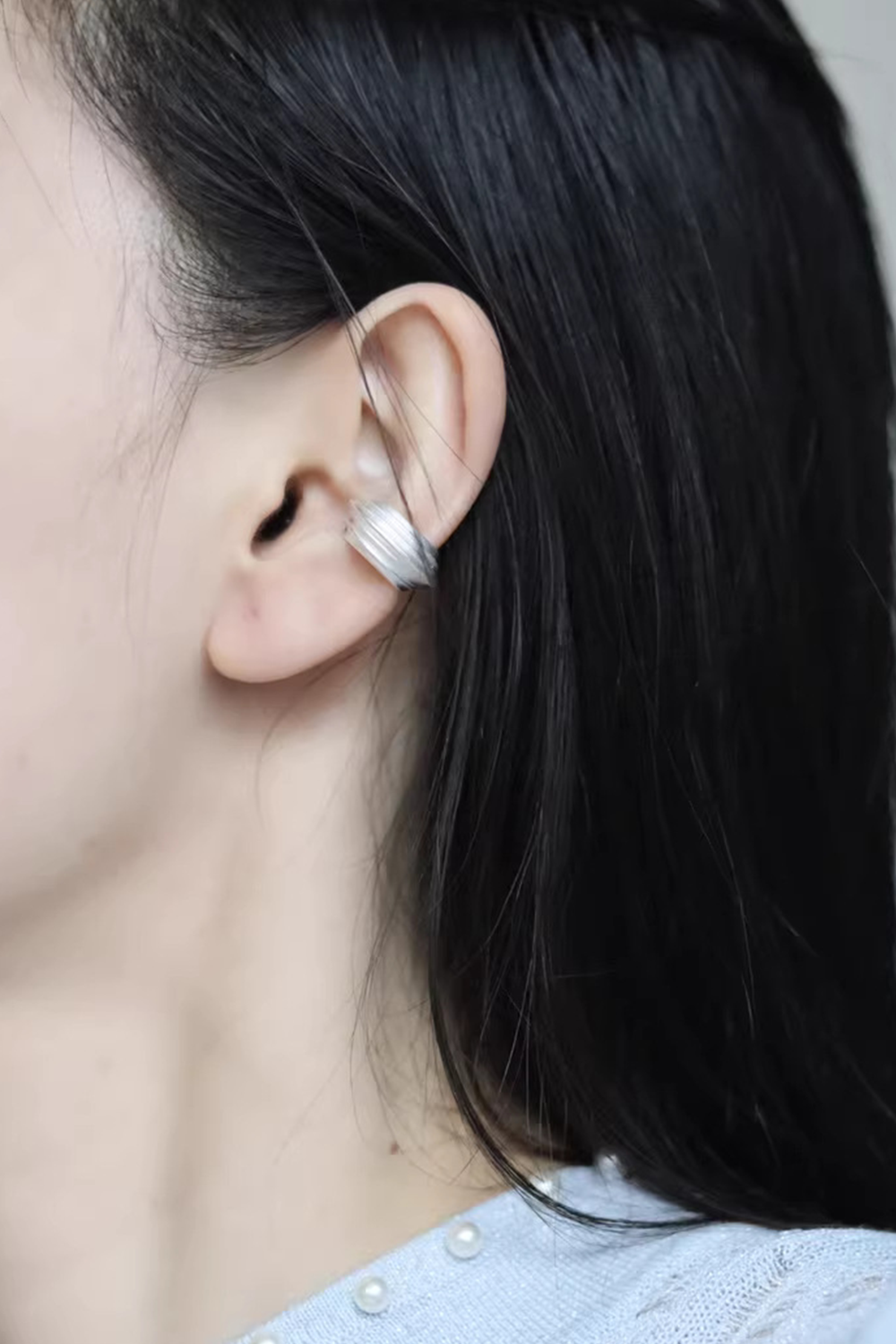 Black-haired woman wearing silver wave ear cuff - Light knit sweater & pearl accents