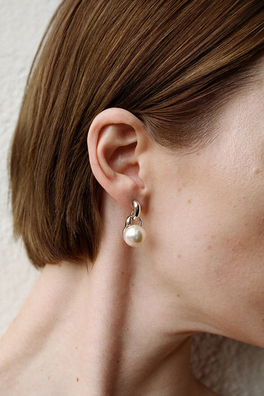 Brown-haired woman wearing teardrop pearl earrings - Close-up with neutral background