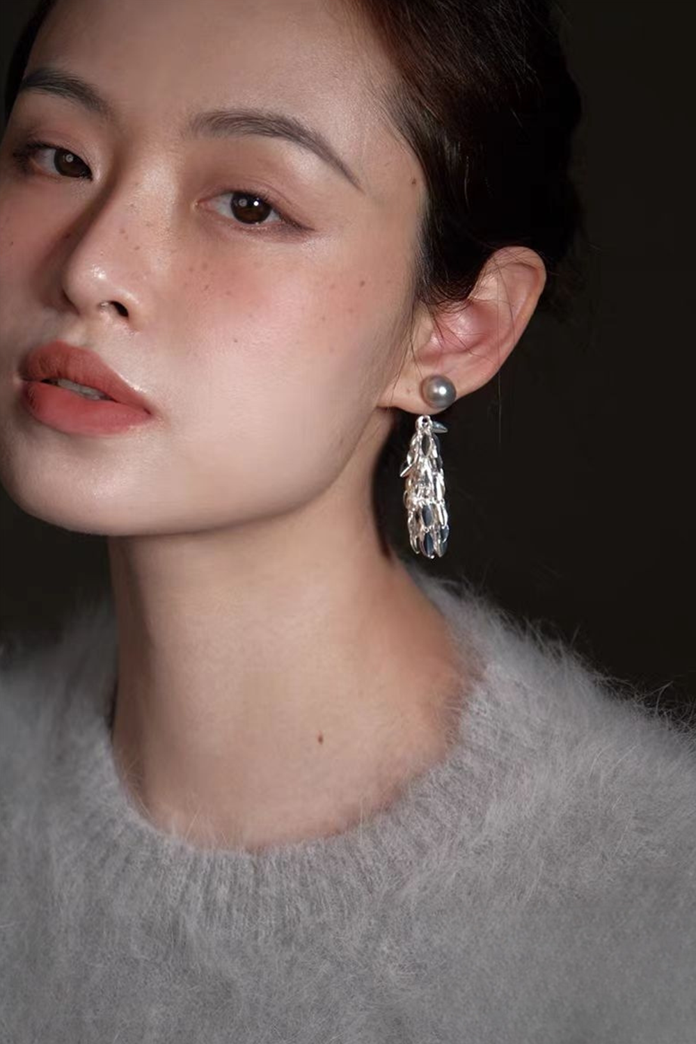 Woman's ear closeup: Gunmetal pearl tiered tassel earrings + heathered gray sweater